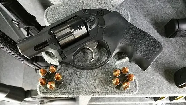 Top-down view of a Ruger LCR revolver with hollow-point ammunition on a grey foam mat.