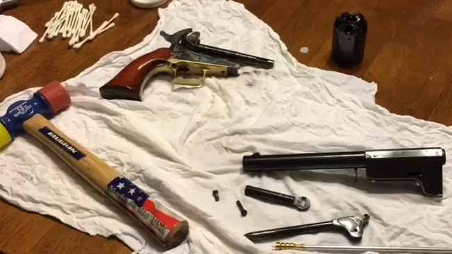 Disassembled Uberti 1851 Navy revolver with parts and gunsmithing tools spread out on a white cloth.