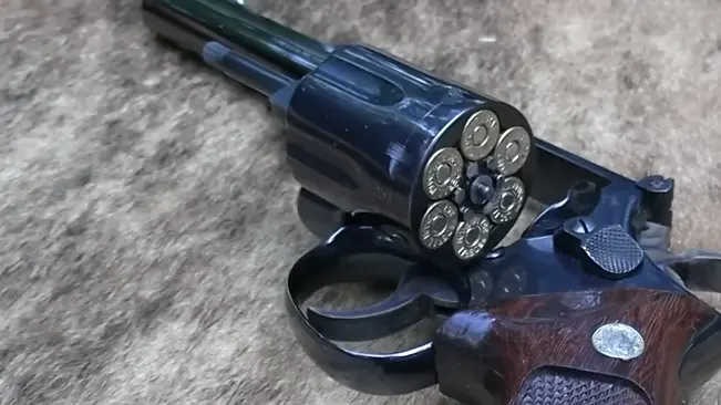Smith & Wesson Model 19 revolver with open cylinder showing six bullets, placed on a textured surface.