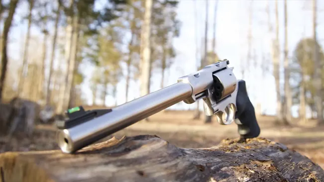 Ruger Super Redhawk revolver with a long barrel, positioned on a fallen log in a forest setting.