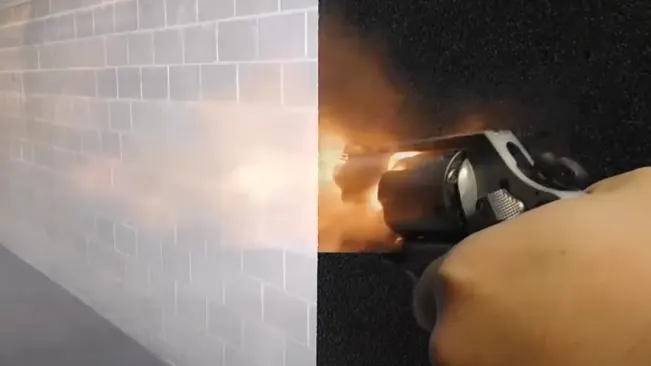 Smith & Wesson M637 revolver discharging with visible muzzle flash against a brick wall.