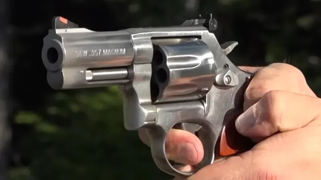 Hand holding a Smith & Wesson 686 Plus Deluxe revolver with the .357 Magnum label visible, outdoors.