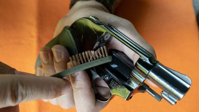 Hand cleaning the cylinder of a S&W Model 49 Bodyguard revolver with a brush.