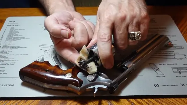 Hands cleaning the cylinder of a Smith & Wesson 686 Plus Deluxe revolver on a schematic mat.