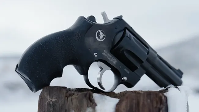 Korth Nighthawk Mongoose revolver resting on a snow-covered wooden stump, with a blurred winter background.