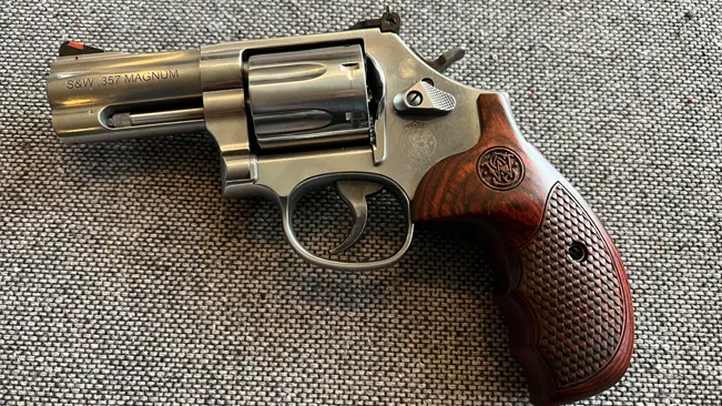Smith & Wesson 686 Plus Deluxe revolver with wooden grips and .357 Magnum engraving on a textured surface.