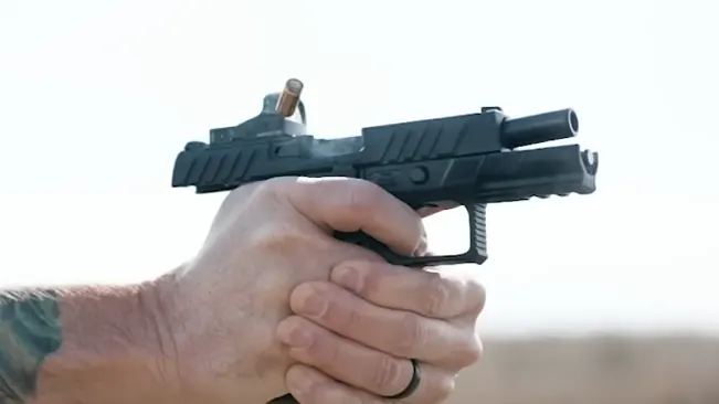 Hand holding a Beretta APX pistol with a mounted optic, ready to fire.