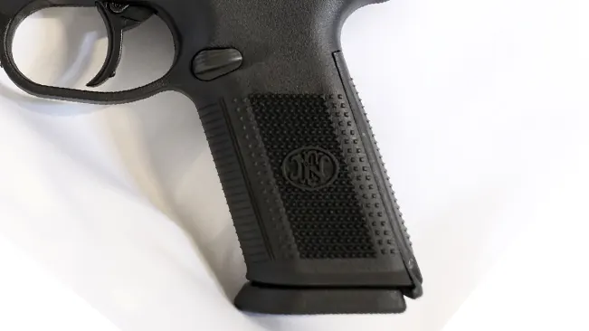 Close-up of the FN logo on the textured grip of an FN FNX-9 pistol against a white background.