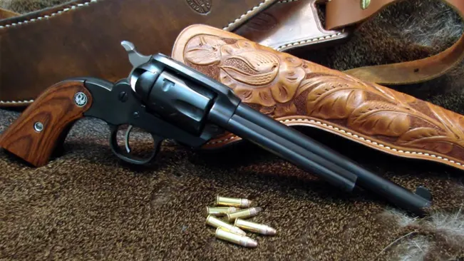 Ruger Bearcat .22 revolver with wooden grips beside ammo, on fur with a tooled leather holster.