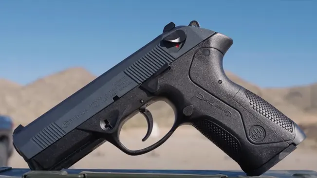 A Beretta PX4 Storm subcompact pistol propped up against a blue sky background, emphasizing its profile and design features.