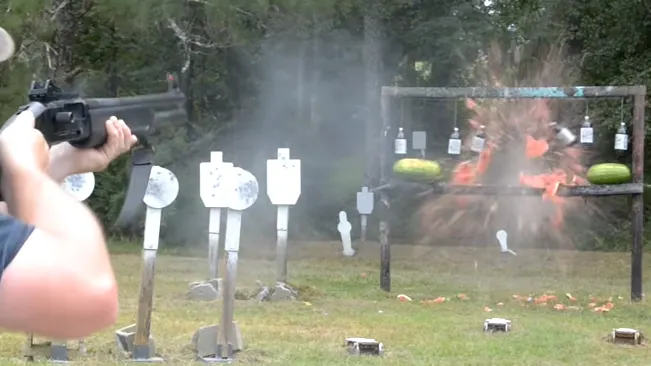 Person in a shooting stance aiming a shotgun at exploding targets on a range