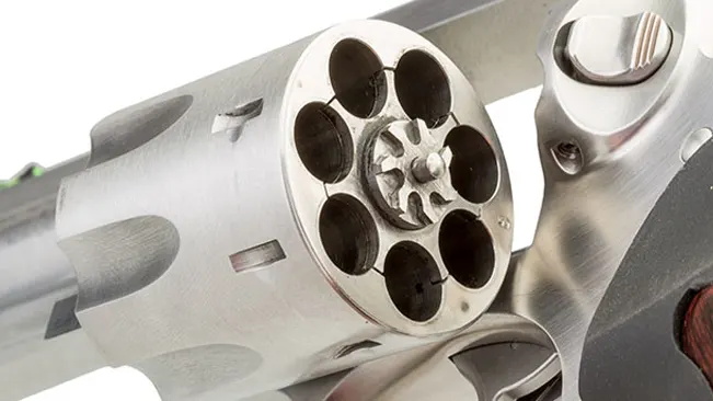 Close-up of the cylinder and extractor of a Ruger GP100 revolver, showing the empty chambers.