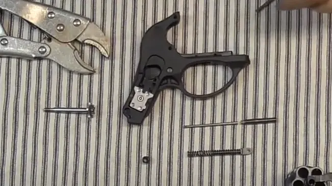 Disassembled Ruger LCR revolver frame and parts with tools on a striped mat.