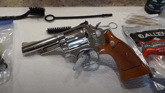 Smith & Wesson Model 19 revolver on a white surface with cleaning supplies, including brushes and cotton swabs, in the background.