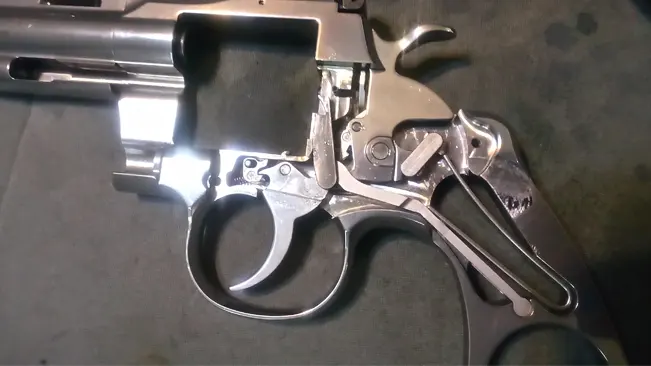 Disassembled Colt Python 3-inch revolver with exposed internal mechanism on a dark surface.