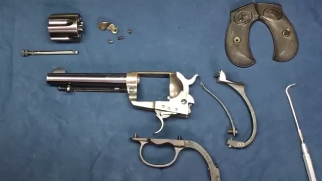 Disassembled parts of a Colt 1877 Thunderer revolver laid out on blue background.