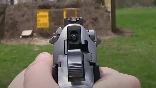 First-person view of aiming a Beretta 92FS INOX pistol, with the front and rear sights aligned on a target range.
