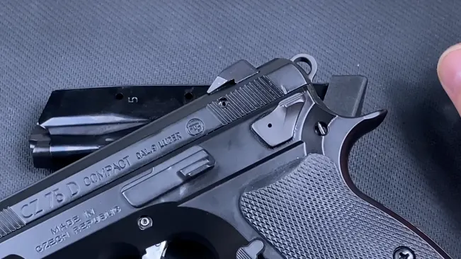 Hand holding a disassembled CZ-75 PCR compact pistol, showing the slide and frame against a textured background.