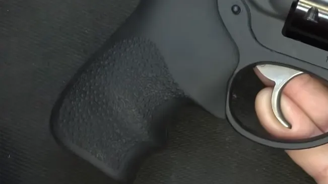Person's hand gripping the textured handle of a Ruger LCR revolver with a visible trigger.
