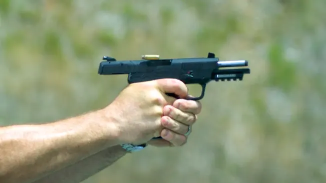 Hand holding an FN Five-SeveN pistol with a cartridge ejecting in mid-fire.