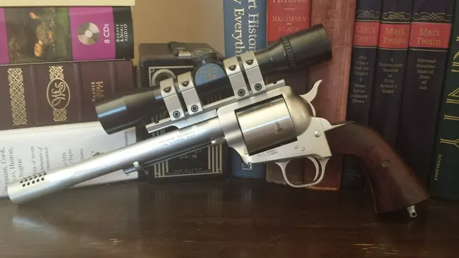 A Freedom Arms Model 83 revolver with a long barrel and scope, resting on a bookshelf among literary works.