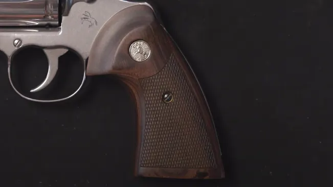 Detailed view of the wooden grip and emblem on a Colt Python 3-inch revolver against a dark background.