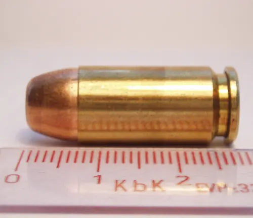 Close-up of a copper-jacketed 9mm bullet over a measuring scale, compatible with a Beretta PX4 Storm subcompact pistol.