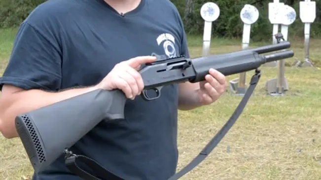 Person holding a Mossberg 930 shotgun with a target backdrop