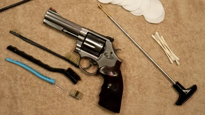 Smith & Wesson 686 revolver with cleaning tools such as brushes, rods, and swabs spread out on a carpet.