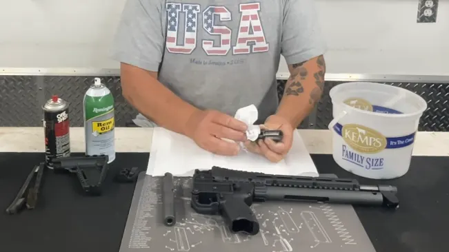Person cleaning a disassembled Kel-Tec SUB-2000 rifle on a workbench with cleaning supplies and parts laid out