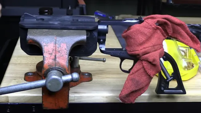 A Freedom Arms Model 83 revolver mounted in a vise on a workbench, with a cleaning cloth and safety glasses nearby.