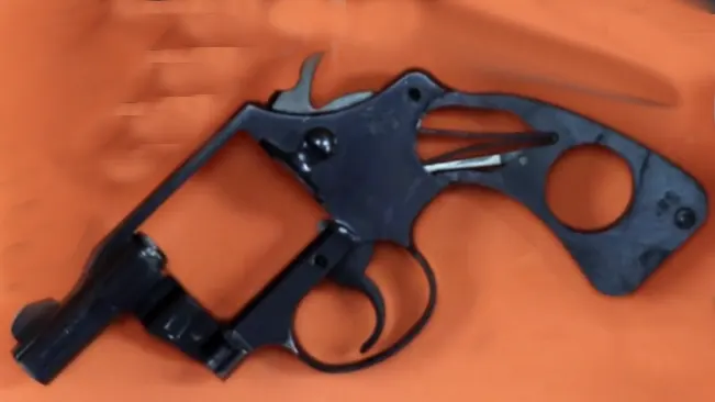 Disassembled Colt Detective Special revolver frame on an orange background.