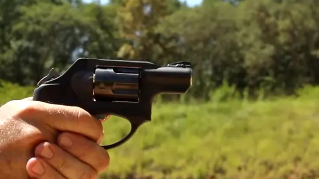 Hand holding a Ruger LCR revolver aimed outdoors with a natural, blurred background.