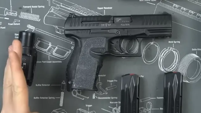Walther PPQ M2 on a schematic mat with magazines and a hand to the side.