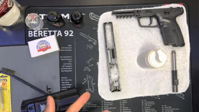 FN Five-SeveN pistol during cleaning, with parts laid out on a mat with Beretta 92 diagram.