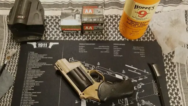 Cleaning and maintenance setup for a handgun with cleaning supplies and ammunition boxes on a mat with a schematic of a 1911