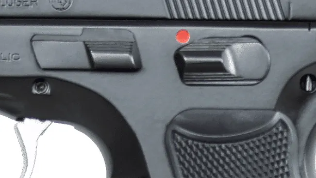 A close-up of a CZ 75 B handgun's safety mechanism, engaged with a red indicator, and detailed texture on the grip.