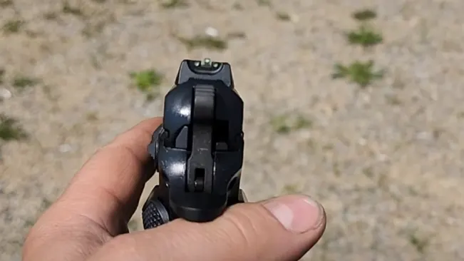 A person's hand is holding a CZ 75 B handgun, shown from the front with the focus on the barrel and front sight.