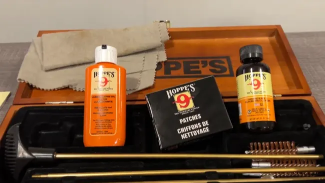 Gun cleaning kit with Hoppe's 9 solvent, lubricating oil, patches, and tools on a wooden tray.
