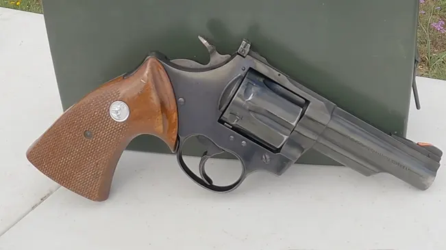 Colt Trooper MK III revolver with wooden grips lying against a green background.