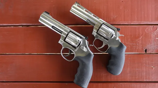 Two King Cobra Target .22 revolvers with stainless steel finishes and black grips on a red wooden surface.