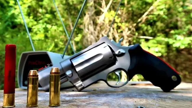 A Taurus Raging Judge 513 revolver with ammunition and a shooting chronograph in the background, outdoors on a wooden surface.