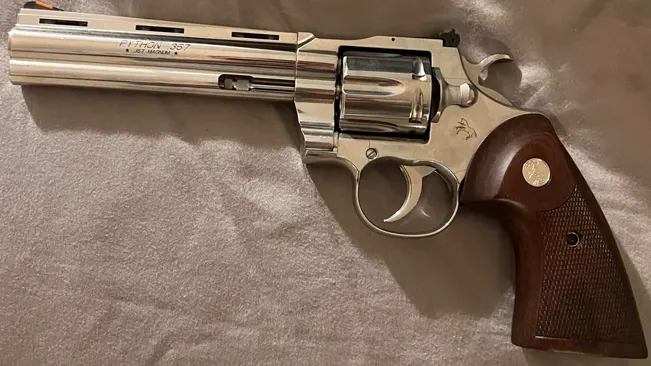 Colt Python 6-inch revolver with stainless steel finish and checkered brown grip on a beige fabric surface.