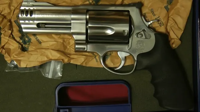 Smith & Wesson Model 500 revolver with a stainless steel finish on a yellow cloth, next to a blue case.