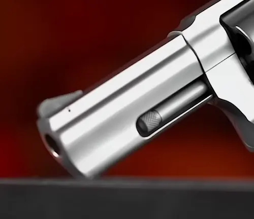 Close-up of the ejector rod and underlug of a Taurus 856 Executive Grade revolver with a red background.