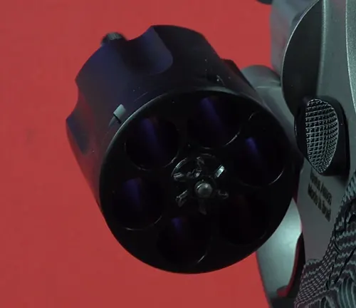 Close-up of the cylinder of a Taurus Defender 856 revolver against a red background.