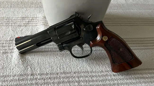 Smith & Wesson Model 586 revolver with a blued finish and checkered wooden grips on a textured surface.