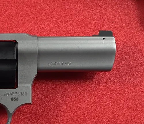 Detail of the barrel and front sight of a Taurus Defender 856 revolver on a red background.