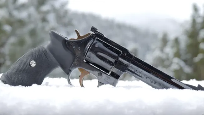 Manurhin MR73 revolver with blued finish and gold-colored accents, resting on snow.