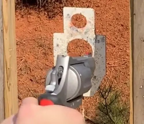 Hand holding a Taurus Raging Judge 513 revolver aimed at a metal target with a dirt background.